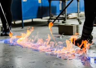 Students drip strings of molten glass into flames fueled by a line of flammable liquid on the floor during a UW Glass Lab event in the Art Lofts Building at the University of Wisconsin-Madison. The public event featured students from the UW Mad Gaffer team performing a number of interesting glass experiments.