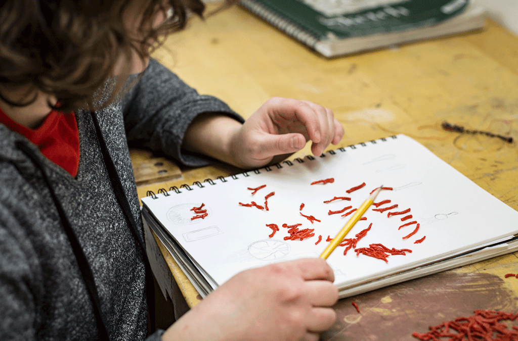 UW-Madison graduate student Chloe Darke, a participant in "Radical Jewelry Makeover: Wisconsin," sketches ideas for new jewelry she could make from pieces of old coral. The project promotes the ethical sourcing of materials through recycling and reuse.